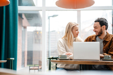 Happy couple hugging and using laptop while drinking coffee in cafe