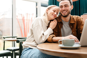 Happy couple hugging and using laptop while drinking coffee in cafe