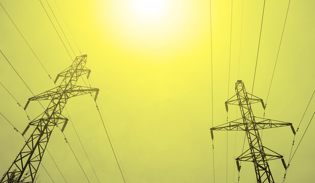 Bottom view of two high voltage pillars and yellow sun against gray sky background