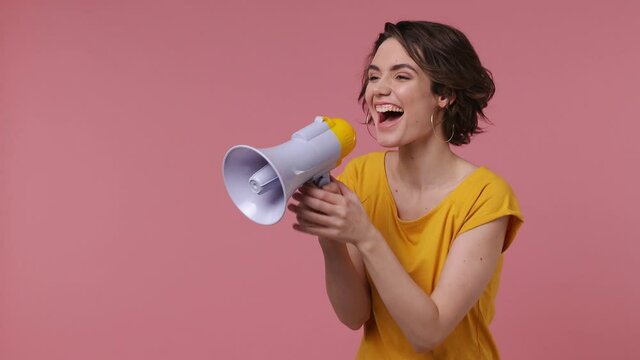 Surprised shocked excited fun young woman 20s wears basic casual yellow t-shirt point index finger aside scream in megaphone announces discounts sale Hurry up isolated on pastel pink background studio