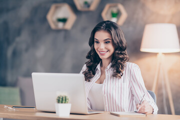 Photo portrait of businesswoman working on laptop sitting in office taking notes smiling