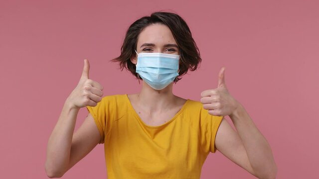 Young woman wear basic casual yellow t-shirt point on sterile face mask ppe to safe from coronavirus virus covid-19 flu on lockdown quarantine show thumb up isolated on pastel pink background studio