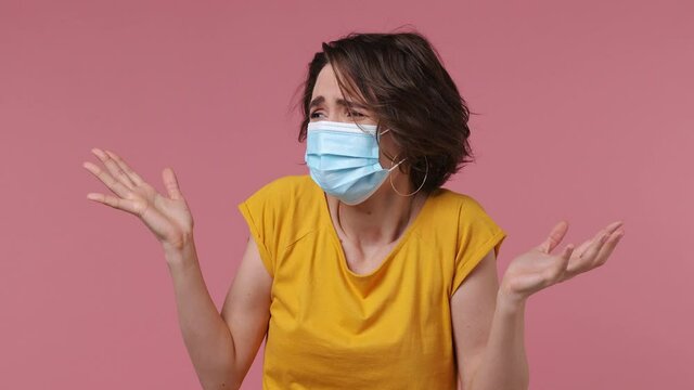 Young shocked woman wear basic casual yellow t-shirt sterile face mask ppe to safe from coronavirus virus covid-19 flu on lockdown quarantine put hand on head isolated on pastel pink background studio