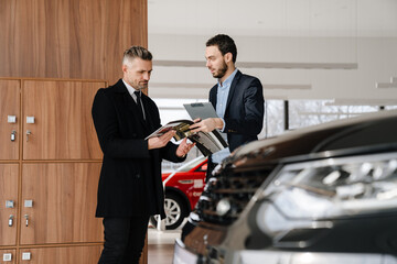 Mid unshaven manager working with mature customer in car showroom
