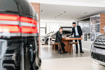 Mature man talking on cellphone while choosing car in showroom
