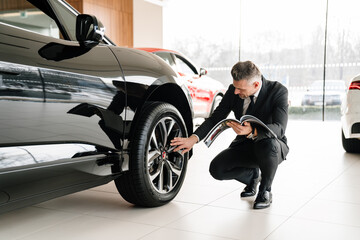 Mature white man choosing and examining car in showroom