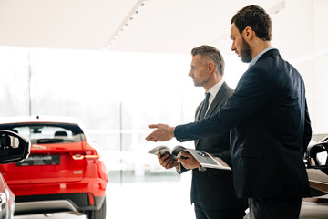 Mid unshaven manager working with mature customer in car showroom