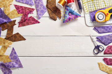 Pieces of fabric sewn in the shape of the letter Z, stacks of multi-colored pieces of fabric, pincushion, quilting and sewing accessories on a white surface