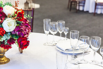 Fancy table set for dinner with flower composition in restaurant, luxury interior background. Wedding elegant banquet decoration and items for food arranged by catering service on white table.