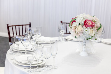 Fancy table set for dinner with flower composition in restaurant, luxury interior background. Wedding elegant banquet decoration and items for food arranged by catering service on white table.