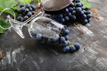 Wine glasses full of grapes on black stone table. Grape bunches with leaves and vines on dark...