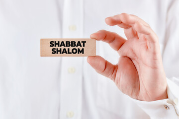 Male hand holds a wooden block with the message Shabbat Shalom.