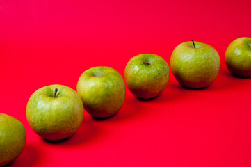 Large green apples, ripe and juicy. Photographed against a uniform red background.