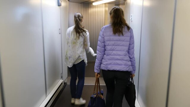 Friends walk to terminal from airliner, woman with little baby turn back and smile. Passengers arrive to destination or change flight, come through jet bridge directly to airport building