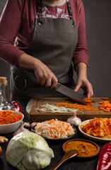 Home cooking. A kitchen table where a woman slices vegetables on a wooden board for fermentation and salting. Vertical orientation, no face