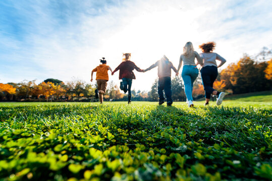 Group of multiracial people holding hands running in the park - Happy friends having fun together outdoor on sunset - People and community concept