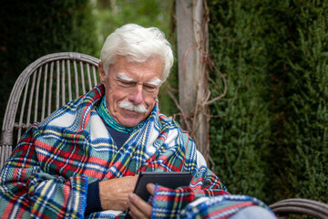 Senior man reading a book on his e-book reader when sitting in the rocking chair.  Portrait of a happy, retired man reading a book on his device.
