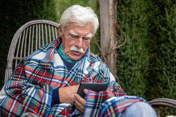 Senior man reading a book on his e-book reader when sitting in the rocking chair.  Portrait of a happy, retired man reading a book on his device.

