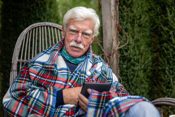 Senior man reading a book on his e-book reader when sitting in the rocking chair.  Portrait of a happy, retired man reading a book on his device.
