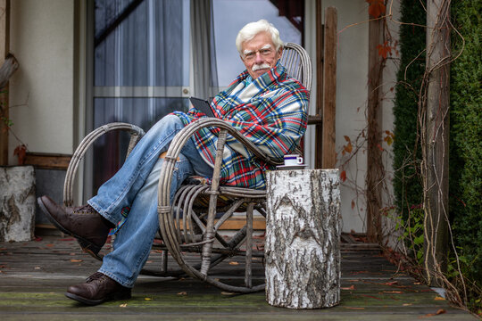 Senior man reading a book on his e-book reader when sitting in the rocking chair.  Portrait of a happy, retired man reading a book on his device.
