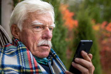 An elderly gentleman is having a phone call. Senior man sitting in the rocking chair during his smartphone conversation. Mature man using his cellular on the veranda.
