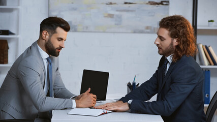 Fototapeta na wymiar young businessmen in formal wear talking near laptop in office