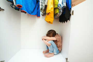 Sad boy hiding in the wardrobe. Domestic violence and abused concept. Unhappy childhood.