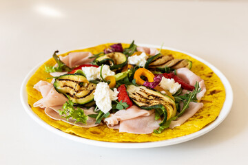 Turmeric flatbread with ham cheese and grilled vegetables on a white background.