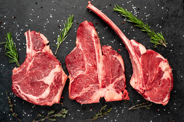 Three raw beef steaks for grilling - rib-eye steak, T-Bone steak, Tomahawk steak on stone background