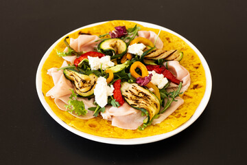 Turmeric flatbread with ham cheese and grilled vegetables on a black background.