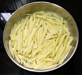 Chopped raw potatoes in a round baking pan. Top view, selective focus
