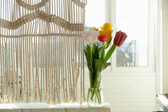 Beautiful spring multicolored tulips in a light interior next to macrame. High quality photo