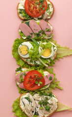 Homemade sandwiches with white bread, vegetables, meat and parsley on a pink background