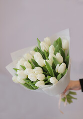 Young woman florist holding big beautiful blossoming mono bouquet of white tulips flowers wrapped in paper. 