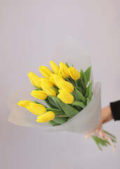 Young woman florist holding big beautiful blossoming mono bouquet of yellow tulips flowers wrapped in paper.