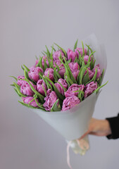 Naklejka premium Young woman florist holding big beautiful blossoming mono bouquet of purple peonies tulips flowers.