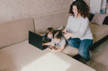 two little girls play on a laptop while lying on the couch mom does her daughter's hair.