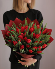 Young woman florist holding big beautiful blossoming mono bouquet of red tulips flowers.