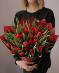 Young woman florist holding big beautiful blossoming mono bouquet of red tulips flowers.