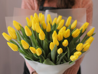 Young woman florist holding big beautiful blossoming mono bouquet of yellow tulips flowers.