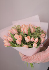 Young woman florist holding big beautiful blossoming bouquet of salmon tulips flowers with greenery