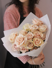 Young woman with a gift bouquet of nude sand roses. Young woman holding fresh bouquet of roses wrapped in light paper.