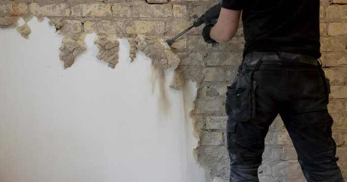 worker removing plaster from indoor brick wall with sds drill