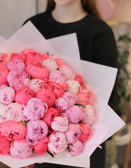 Very big bouquet of pink and white peonies. Young woman holding fresh beautiful bouquet of peony wrapped in paper. Flower gift.