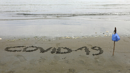 text COVID19 written on the sea beach and the flag made with a s