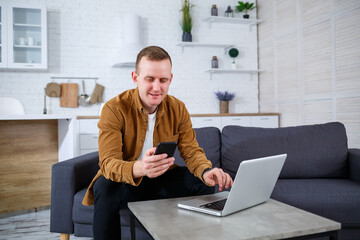 Young successful man is sitting at home on the couch with a laptop and working. Remote work during quarantine.