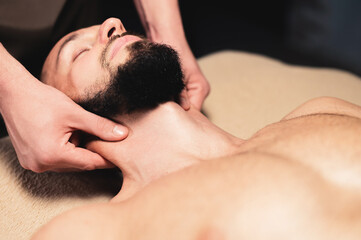 Close-up Professional neck massage to a bearded male athlete in a dark room of a spa massage room