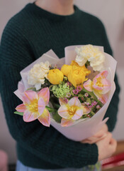 Young woman holding small delicate flower bouquet-compliment. Bouquet of fresh beautiful flowers wrapped in paper. Mother`s day.