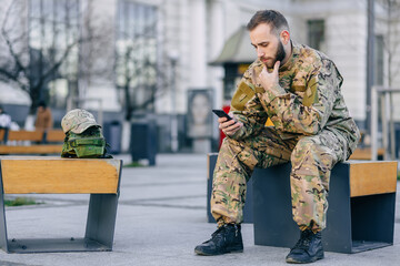 Fototapeta premium handsome male soldier in uniform sits on a park bench looking at
