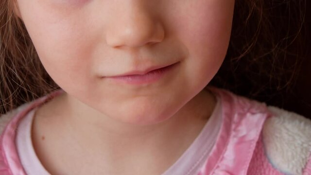 Cute preschooler child wobbling her lower milk tooth and smiling. Deciduous tooth replacement by permanent 4k footage dark background. Scared little girl 6-7 years old has lost incisor.